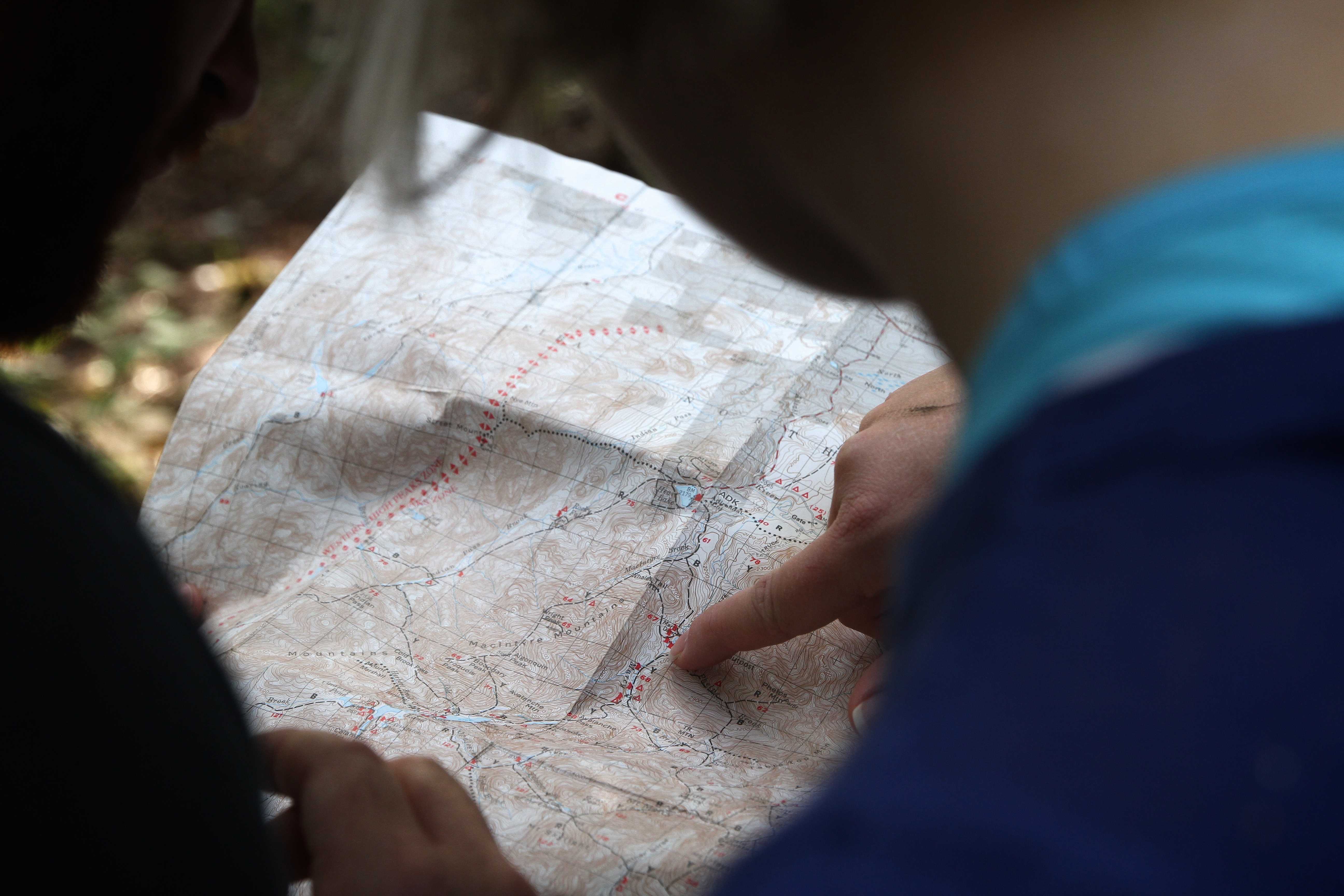 Persona señalando ruta en mapa topográfico con curvas de nivel y caminos marcados
